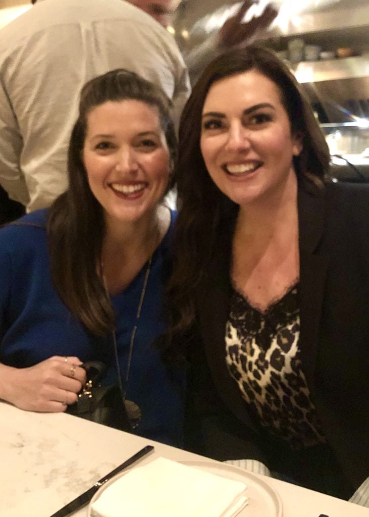 Two brunette women sitting side-by-side at a restaurant smiling
