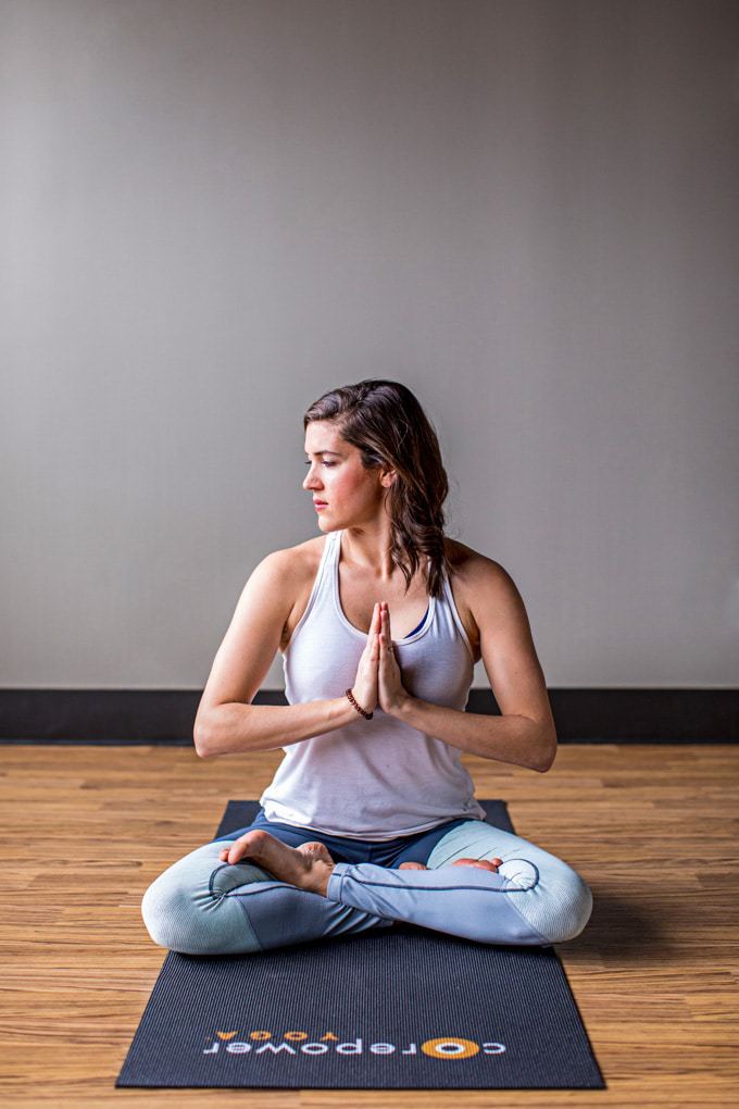 A woman on a yoga mat with crossed legs and hands in prayer position.