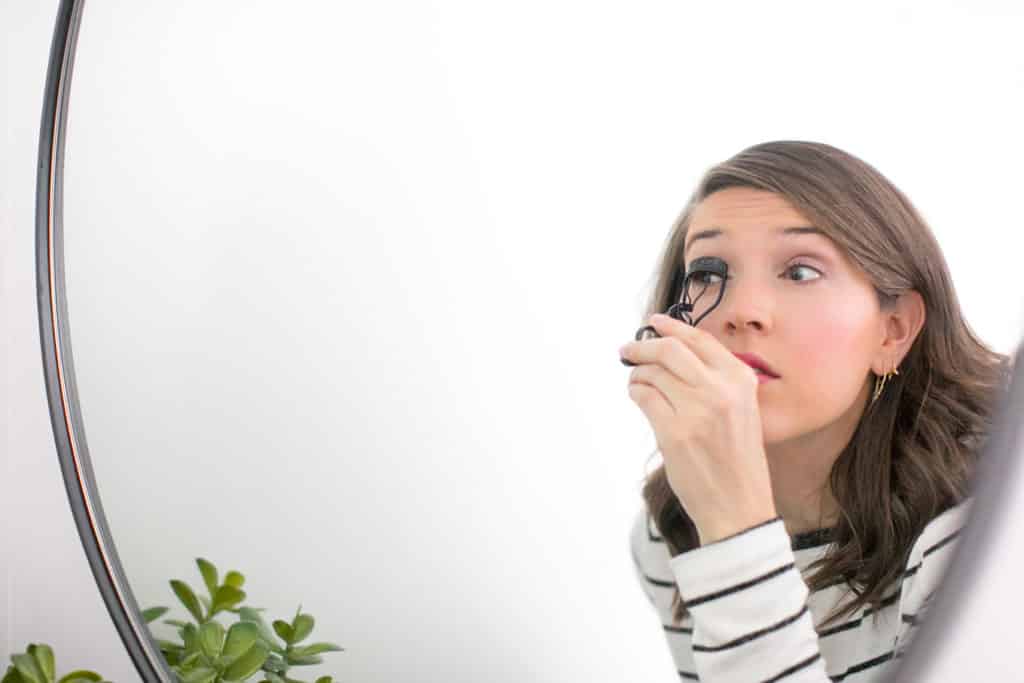 White woman doing eye makeup in a mirror 